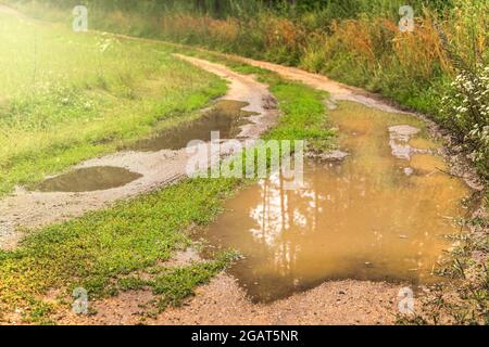 Große Pfützen auf der Straße nach Regen im Sommer. Schlammige Feldstraße mit einer Pfütze in der tschechischen Landschaft. Wasser auf dem Weg. Stockfoto
