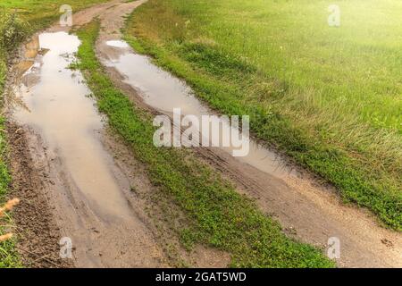 Große Pfützen auf der Straße nach Regen im Sommer. Schlammige Feldstraße mit einer Pfütze in der tschechischen Landschaft. Wasser auf dem Weg. Stockfoto