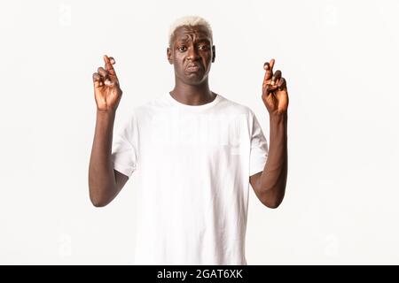Porträt von ängstlich und traurig afroamerikanischen blonden Mann, schmollend und Kreuzfinger viel Glück, machen Wunsch, weißer Hintergrund Stockfoto