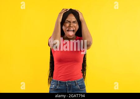 Emotionale Afrikanisch-Amerikanische Lady Schreit Laut Rührenden Kopf, Der Über Dem Hintergrund Des Gelben Studios Steht. Aufnahme Einer Schwarzen Millennial-Frau, Die Mit Schrie Stockfoto