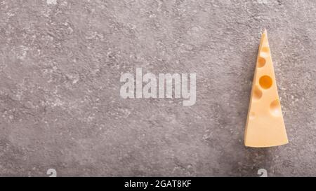 Ein Stück Maasdam-Käse mit großen Löchern auf grauem Betongrund. Nahaufnahme Stockfoto