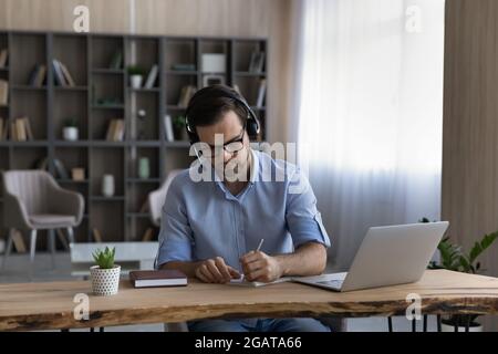 Der junge Student trägt Kopfhörer mit Handschrift vor dem bildschirm des pcs Stockfoto