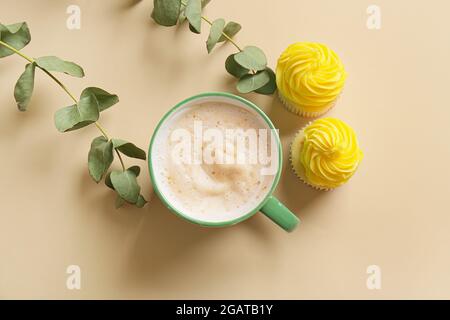 Tasse Kaffee mit Cupcakes und Pflanzenzweigen auf farbigem Hintergrund Stockfoto