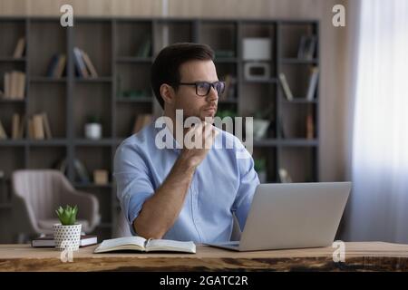 Smart junge Kerl Student Pass Prüfung mit Laptop denken erwägen Stockfoto