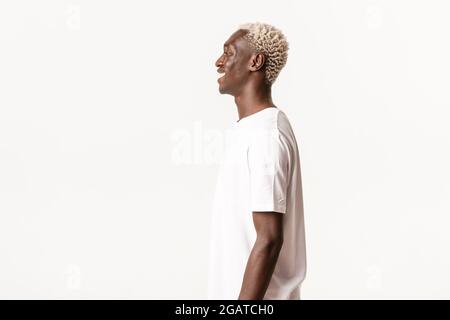 Profil von fröhlich gut aussehenden afroamerikanischen blonden Kerl, lacht und lächelt glücklich auf der linken Seite, stehen weißen Hintergrund Stockfoto