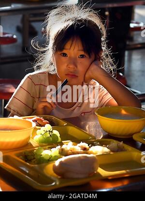 Zhengzhou, Chinas Provinz Henan. Juli 2021. Ein Mädchen hat ein Abendessen an einem vorübergehenden Umzugsort in einer Mittelschule im Bezirk Xunxian der Stadt Hebi, in der zentralchinesischen Provinz Henan, 29. Juli 2021. Mehr als 13.91 Millionen Menschen in 150 Regionen auf Kreisebene waren von der letzten Regengüsse seit Juli 16 betroffen. Kredit: Li An/Xinhua/Alamy Live Nachrichten Stockfoto