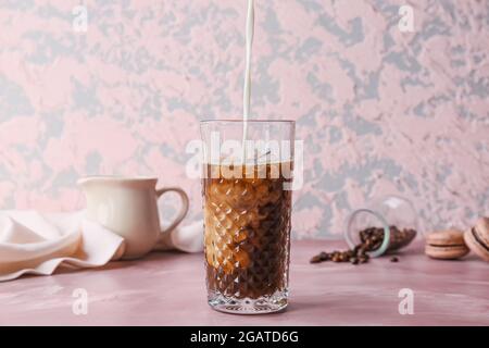 Gießen von Milch in Glas mit heißem Kaffee auf farbigem Hintergrund Stockfoto