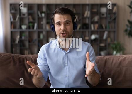 Bärtiger Business Trainer in Kopfhörern schaut sich das Webinar an, in dem die Kamera gehalten wird Stockfoto