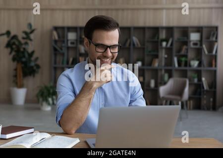 Lächelnder, intelligenter junger Mann sitzt am Laptop im wissenschaftlichen Labor Stockfoto