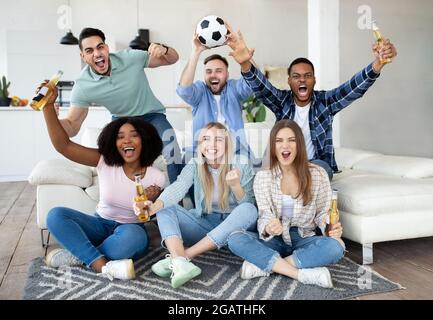 Begeisterte verschiedene Freunde, die Fußball gucken, Fußball halten, Tore rufen, den Sieg feiern und für ihre Lieblingsmannschaft zu Hause jubeln. Gruppe von Stockfoto