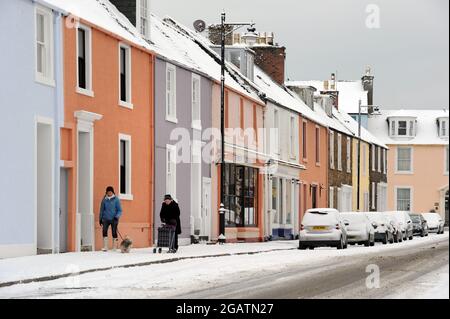 Eine Straße in Kirkcudbright, Dumfies und Galloway, Schottland. Die Häuser sind farbenfroh und der Winterschnee liegt auf der Straße und auf dem Straßenbelag Stockfoto