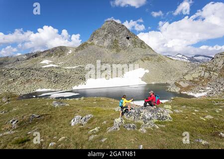 Mutter und Sohn sitzen auf einem großen Felsen beim Wandern am Pfringer See, Österreich Stockfoto