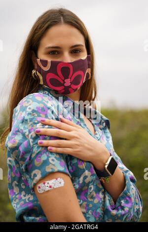 Junge Frau, die einen Arm mit einer Haftbandage zeigt, um die Impfung gegen das Coronavirus Covid-19 zu beweisen. Konzept der geimpften Menschen Stockfoto