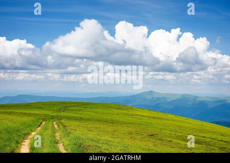Berglandschaft an einem sonnigen Tag. Trail durch grasbewachsene Wiese. Schöne Reiseszenerie. Grat in der Ferne unter einem blauen Himmel mit atemberaubenden Wolken Stockfoto