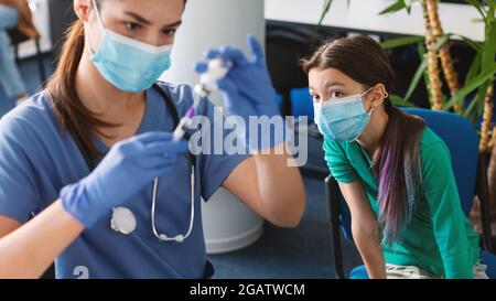 Impfkonzept. Krankenschwester Füll Spritze entnehmen Medikamente aus dem Fläschchen, bevor sie Jab. Selektiver Fokus auf jugendliches Mädchen, das auf Cov wartet Stockfoto