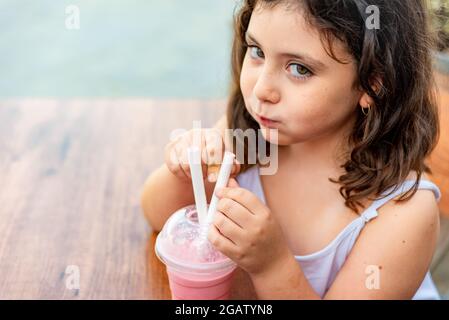 Kleines lateinisches Mädchen, das einen Erdbeermilchshake mit witzigem Gesicht trinkt Stockfoto