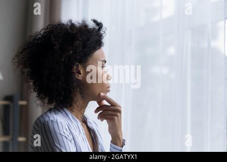 Nachdenkliche afroamerikanische Frau schaut im Fenster und denkt Stockfoto