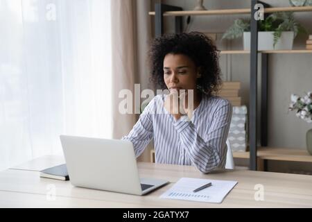 Nachdenkliche afroamerikanische Frau arbeiten online am Laptop Stockfoto