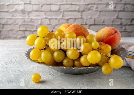 Reife Trauben und Pfirsiche in einer Holzschüssel aus Metall auf einem grauen Tisch. Stockfoto