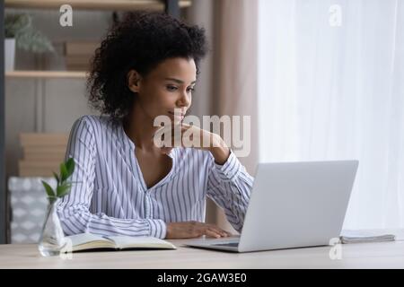 Eine nachdenkliche ethnische Frau sitzt am Schreibtisch auf einem Laptop Stockfoto