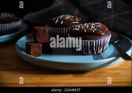 Geburtstagskuchen. Leckere Cupcakes aus Schokolade mit Creme und farbigen Streuseln. Süßer, köstlicher Desserttrüffel und Süßigkeiten auf einem Teller. Weißer Hintergrund wi Stockfoto
