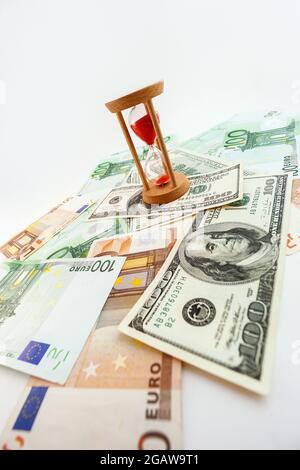 100-Dollar- und Euro-Banknoten mit Sanduhr auf weißem, isoliertem Hintergrund Stockfoto