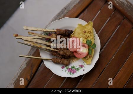 Eine Portion balinesischer Fischsatay mit frischen Tomaten, Sellerie und knusprigen Chips auf einem alten Holztisch. Sieht köstlich und köstlich aus Stockfoto