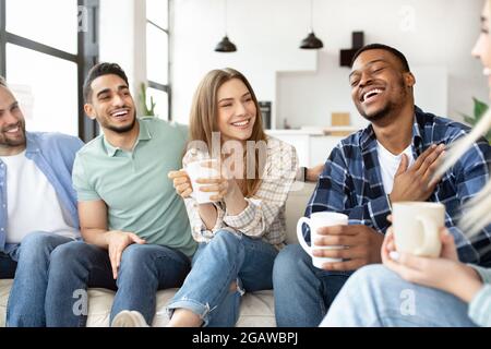 Home Party-Konzept. Eine Gruppe verschiedener Freunde, die am Wochenende gemeinsam Zeit verbringen, heiße Getränke halten, sich unterhalten und lachen. Multirassische Mille Stockfoto