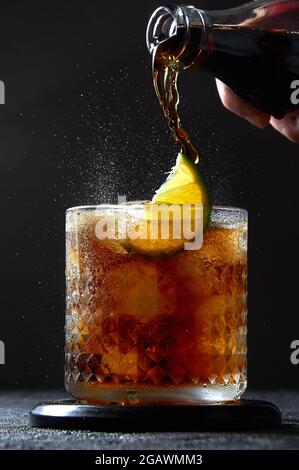 Cuba Libre oder Long Island Cocktail mit Cola, Rum und Limette in Glas. Sodaspray auf dunklem Hintergrund. Erfrischender Sommerdrink. Stockfoto