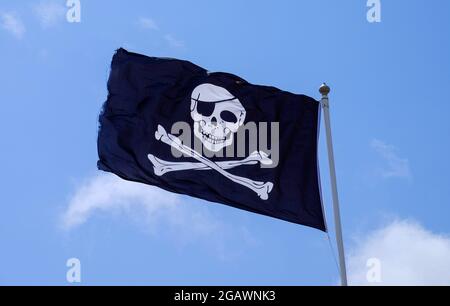 Piratenflagge, auch bekannt als Jolly Roger oder Totenkopf- und Kreuzknochen-Flagge, abgebildet vor einem blauen Himmel. Stockfoto