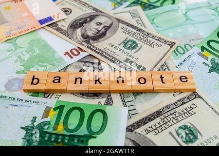 Banknotenbeschriftung auf Holzwürfeln auf der Textur von US-Dollar- und Euro-Banknoten Stockfoto