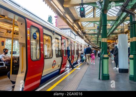 Am Bahnsteig der South Kensington Station befindet sich ein U-Bahn-Zug der Londoner U-Bahn. Die Fahrgäste können dort ein- und aussteigen Stockfoto