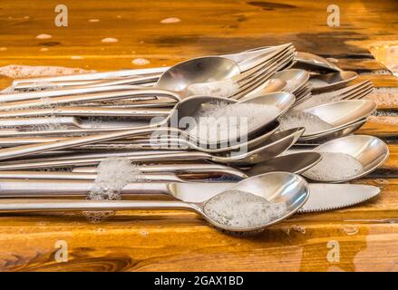 Nahaufnahme aus seifig gewaschenem Stahlbesteck, das auf einem Abtropfbrett aus Holzwaschbecken aufgesteckt wurde. Stockfoto