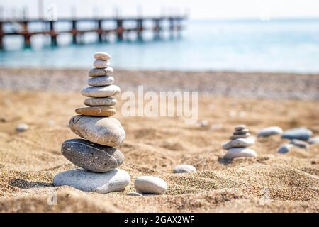 Steinpyramide zur Meditation auf dem Sand auf verschwommenem Meeresgrund liegend. Das Konzept der Entspannung und Erholung. Stockfoto