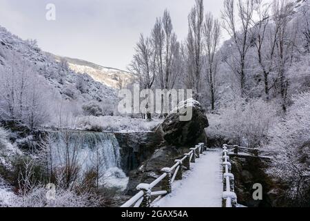 Weiße Landschaft einer Brücke über den Fluss Poqueira mit blattlosen Bäumen nach einem Schneefall. Stockfoto