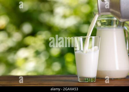 Milch, die aus Metallkännen ins Glas im Freien fließt Stockfoto