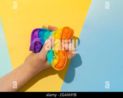 Weibliche Hand mit popit-Spielzeug in die Faust geballt, Draufsicht über zwei Schatten blauen Hintergrund. POPIT auf blauem Hintergrund mit Kopierplatz. Beliebte Silikon bunte Antistress Pop it Spielzeug für Kind. Draufsicht von oben. Einfache Grübchen Stockfoto