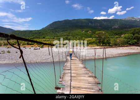 Eine Touristin überquert die alte Hängebrücke über den wunderschönen Fluss Vjosa, in der Nähe von Çarçovë, Nemërçka, Gjirokastra, albanien Stockfoto
