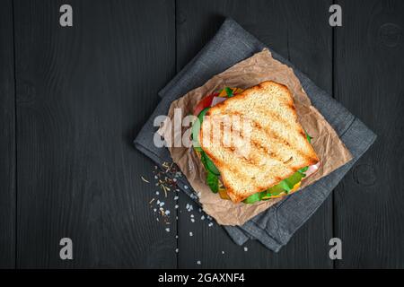 Gegrilltes Sandwich mit Gemüse und Schinken auf schwarzem Hintergrund. Draufsicht, Kopierbereich. Stockfoto
