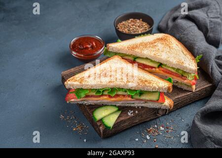 Zwei Sandwiches mit Schinken, Käse, Tomaten, Gurken und Salat auf dunkelgrau-blauem Hintergrund mit Platz zum Kopieren. Seitenansicht. Fast Food. Stockfoto