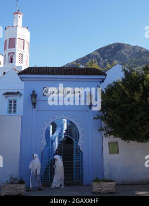 CHEFCHAOUEN, MAROKKO am 2019. APRIL: Eingangstor und zwei arabische Frauen in afrikanischer Stadt, klarer blauer Himmel an warmen sonnigen Frühlingstag am April - vertikal Stockfoto