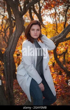 Eine niedliche rothaarige Frau in guter Laune posiert an einem Herbsttag und genießt das schöne Wetter. Das Konzept und die Idee, Herbst und Herbst Getaway zu genießen Stockfoto