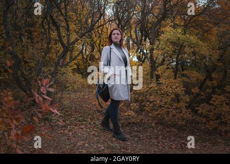 Eine niedliche rothaarige Frau in guter Laune posiert an einem Herbsttag und genießt das schöne Wetter. Das Konzept und die Idee, Herbst und Herbst Getaway zu genießen Stockfoto