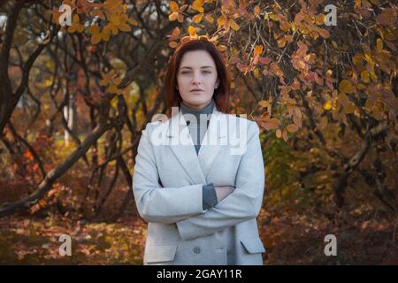 Eine niedliche rothaarige Frau in guter Laune posiert an einem Herbsttag und genießt das schöne Wetter. Das Konzept und die Idee, Herbst und Herbst Getaway zu genießen Stockfoto