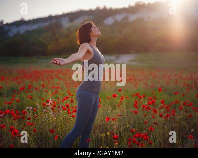 Junge schöne Frau mit erhobenen Armen im Frühjahr Mohnfeld. Sanfte Farben. Nachdenkliche, entspannte Atmosphäre. Stockfoto