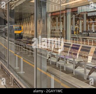 Ein Wartezimmer am Bahnhof mit einem reflektierten Bild eines Zuges auf einem angrenzenden Bahnsteig. Ein weiterer Zug kann durch das Glas gesehen werden. Stockfoto