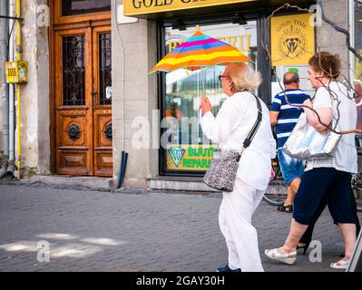 Timisoara, Rumänien - 06.25.2021: Ältere Frau, die einen farbigen Regenschirm hält, um sich an einem heißen Tag vor der Sonne zu schützen, in Timisoara Stockfoto