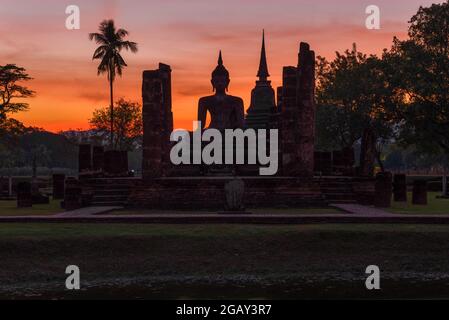 Skulptur von Lord Buddha auf den Ruinen Buddhistischer Tempel von Wat Chana Songkram im Hintergrund des Sonnenuntergangs. Sukhothai, Thailand Stockfoto