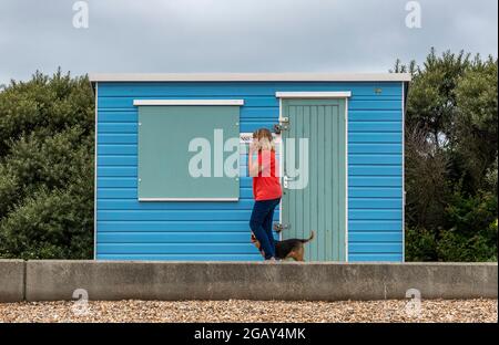 Frau, die mit dem Hund spazieren geht, Frau, die mit dem Hund geht, Frau, die mit ihrem kleinen Hund an der Strandhütte vorbeigeht, Frau mit Hund, Strandhütte. Stockfoto