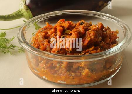 Ein feuergeröstetes Gericht mit Zwiebeln, Tomaten und Gewürzen. Allgemein bekannt in Indien als Baingan bharta. Aufgenommen auf weißem Hintergrund. Stockfoto